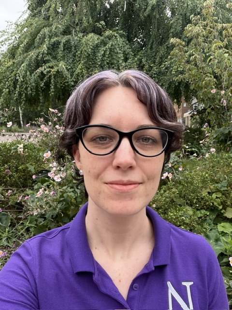 Photo of Chelsea standing outside. She is wearing a purple Northwestern polo, glasses, and and purple streaks in her hair.