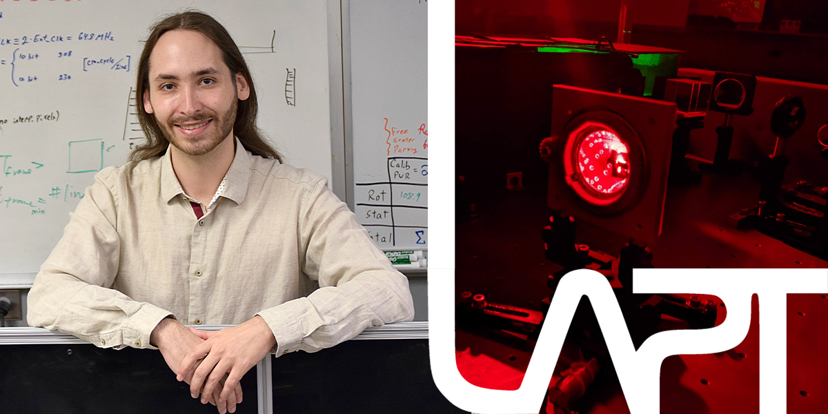 Julian Gamboa González smiling in front of a whiteboard beside a red-lit laboratory setup.