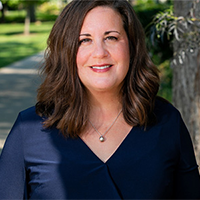 A photo Sarah Klaper wearing a navy shirt, standing outside in front of a tree