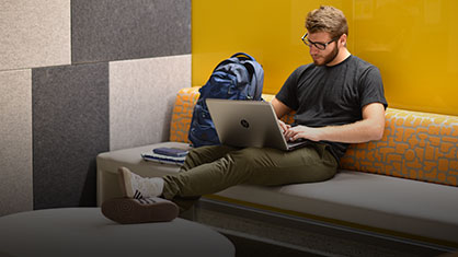 A male student sitting on a couch with his laptop