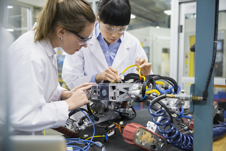 two female students in white lab coats working with wires in a lab